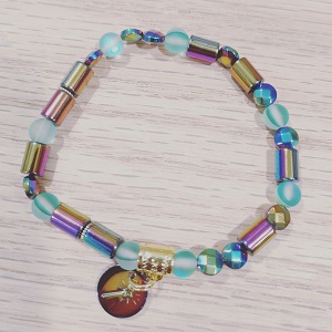 A rainbow colored hematite and glass bead stretchy bracelet that spells out the word "magical" morse code. The attached charm is a magic wand hand-stamped in rainbow stainless steel